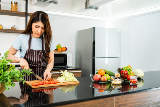 A happy young Asian woman preparing a healthy salad. Cutting vegetables tomatoes and cabbage on a cutting board on the home kitchen counter. Image with copy space.