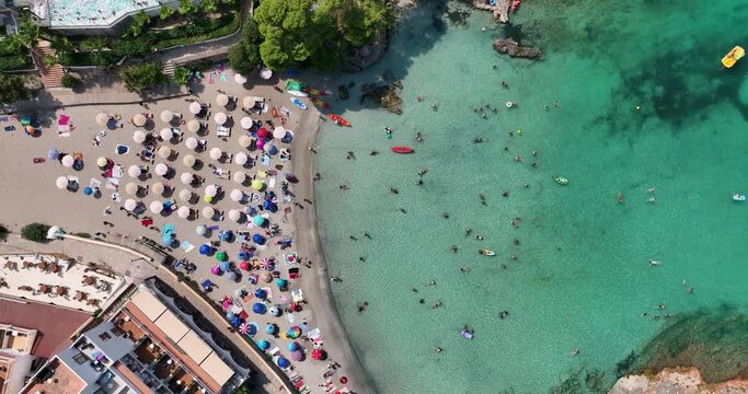 Aerial video of a beach full of people enjoying the sun and crystal clear water. Colored umbrellas and towels.