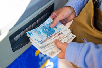 grandmother withdraws her pension at an ATM. A woman holds Polish money and zloty bills in her hands - obrazy, fototapety, plakaty
