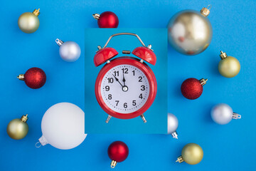 Christmas composition with red alarm clock and colored balls on the blue background. Top view. Closeup.