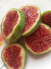 The fruit of a ripe, juicy fig on a white plate with a pattern cut into slices closeup.