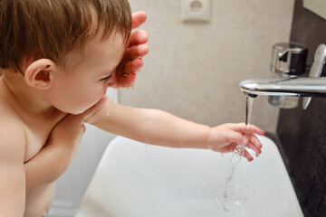 Woman mother washes face of happy toddler baby in sink with faucet. Mom helps with hygiene child boy. Kid aged one year and two months