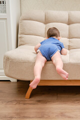 Fototapeta na wymiar Toddler baby climbs on the sofa. Child boy learning to get off the bed. Kid age one year