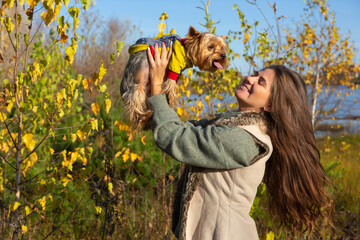 portrait of a woman with a Yorkshire terrier dog in her arms in the autumn forest