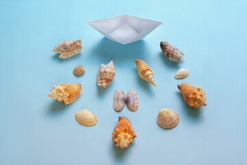 White paper boat and sea shells on blue background. Copy space