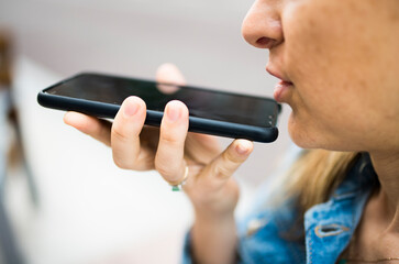 selective view of smart phone of 40 year old woman in the street sending a voice message with the smartphone or consulting with the voice assistant