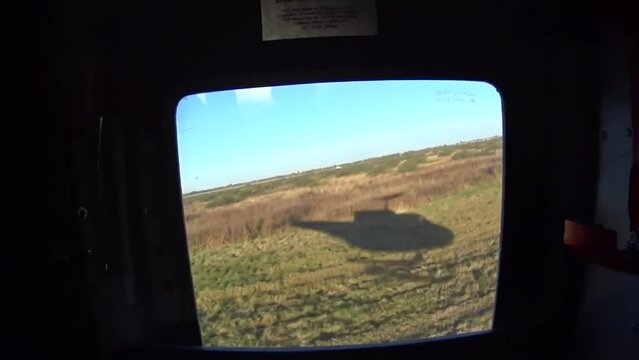 sombra de helicoptero militar proyectada en el pasto vista desde la ventanilla mientras el helicoptero se eleva, al atardecer