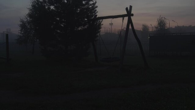Empty swing on children's playground swinging at foggy night. Horrible poltergeist and ghost concept	