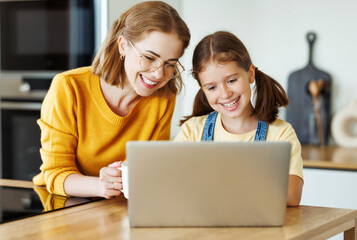 Cheerful girl using a laptop with  her mom    in the kitchen at home