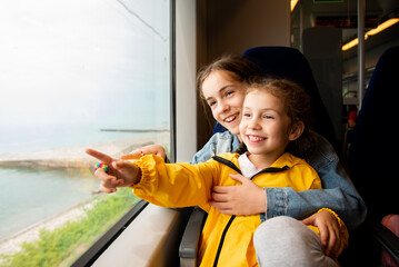 Two sister girls look out the window of a train at the sea.The girls are talking and having fun. Journey. Reflection. Vacation. Summer. Family vacation.