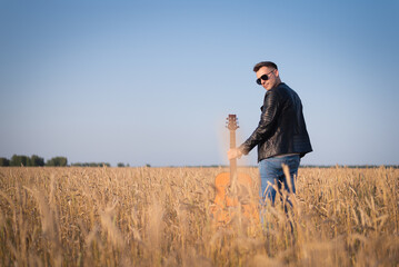 Musician with a guitar is walking among the wheat field.