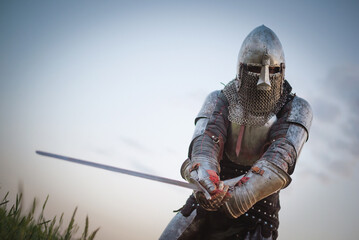 The knight in the plate armor and helmet holds a sword in hands close up.