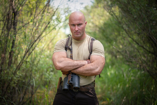 Serious adventurer man standing on the green forest thickets background.