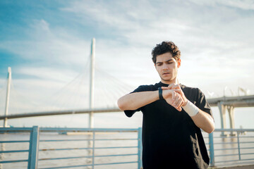 Looks at the fitness watch used for training measuring results. A male trainer does a workout in a tracksuit