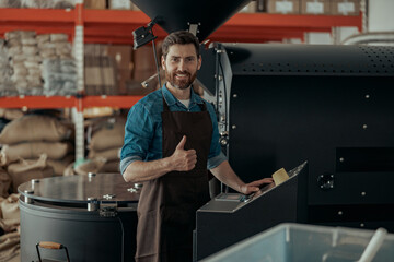 Worker operating of coffee roasted machine on small roasting factory and rise his finger up