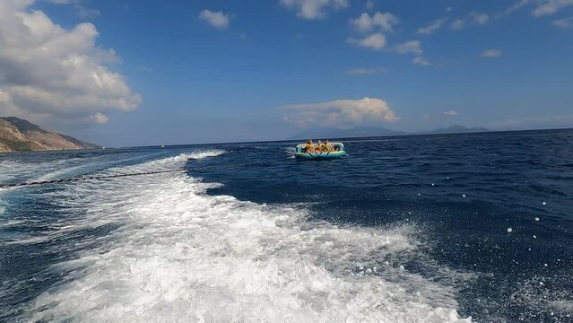 Three people sitting on inflatable tube, behind a speedboat, Kos, Greece, Aegean Sea