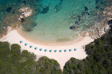 Blue umbrellas along the coastline on the beach top view. Transparent beaches of sardinia aerial...