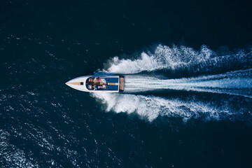 A white large open boat with people is moving quickly on dark water. Top view. White speedboat fast...