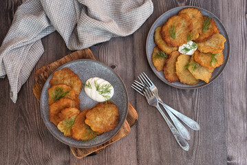 Classic potato pancakes with sour cream sauce served on a gray ceramic dish. Traditional Belarusian potato pancakes draniki on a dark wooden table.