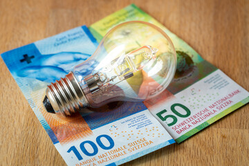 Swiss money 150 francs and a light bulb, concept of rising energy and electricity prices in...