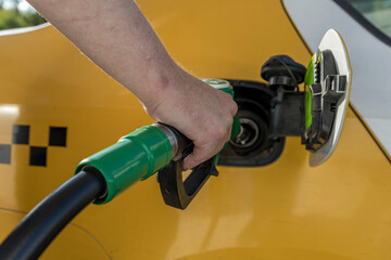 A man refueling a car at a gas station. The taxi driver pours fuel into the tank of the car. A man holds a refueling pistol in his hand.