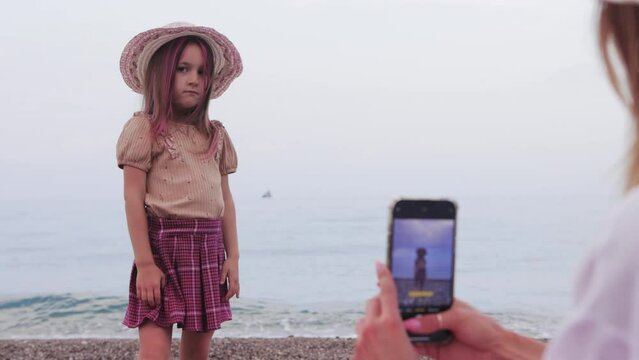 Woman taking pictures of her pretty daughter posing on the background of the sea