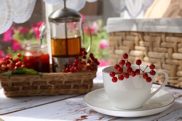 Cup of hot drink and viburnum berries on white wooden table indoors