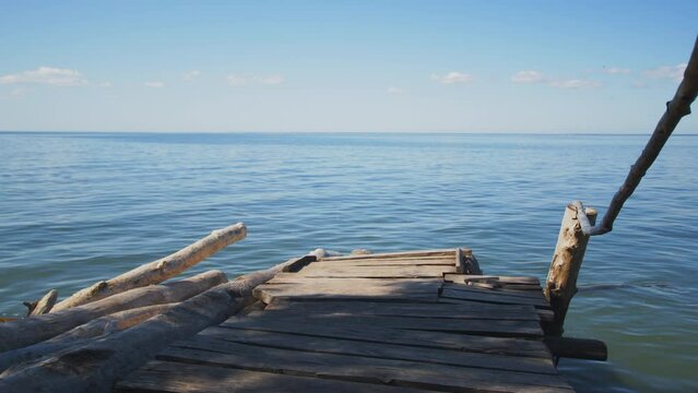 Wooden pier on seashore, calm blue water and clear sky on horizon. Tranquility and relaxation