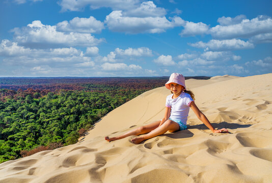 Girl sitting on a huge sand dune, famous tourist destination Dune Pyla. Pilat Dune in France. High quality photo