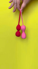 Sex toys. Two geisha balls (red and pink) on a hand. Yellow background. Useful for sex shop, adult