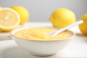 Delicious lemon curd in bowl on white wooden table, closeup