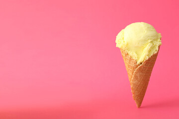 Delicious yellow ice cream in waffle cone on pink background. Space for text