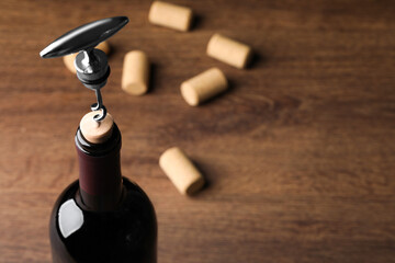 Opening wine bottle with corkscrew on wooden table, closeup. Space for text
