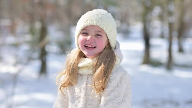 Little cute girl in outerwear, hat and scarf looking at camera and smiling in winter park. Winter time, Care free childhood.