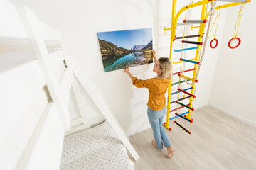 Canvas print with gallery wrap. Woman hangs photography on white wall. Hands holding photo canvas...