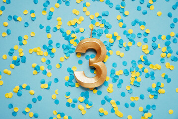 Number 3 three golden celebration birthday candle on yellow and blue confetti Background. three...