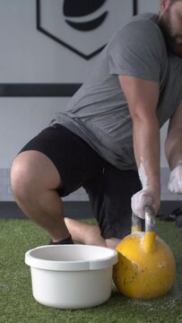 Vertical video.Man getting ready by smearing his hands in magnesium to lift a kettlebell 