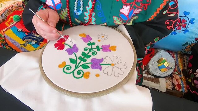 Close-up of the hands of the senior woman, embroidering floral ornament. Ethnic folk embroidery of the Bashkortostan