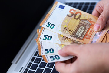 Euro banknotes in female hands on laptop background. Woman counting money, concept of wages or bonus