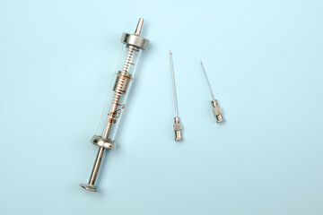 An old-fashioned syringe and two needles on a blue background. Top view, flat lay.