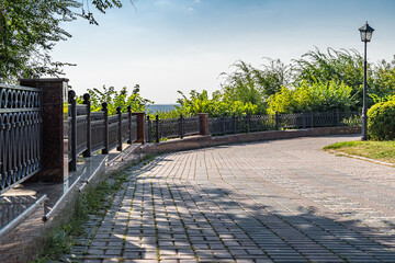 Receding into the distance is a beautiful cast black metal fence along a paving stone path in a city park.