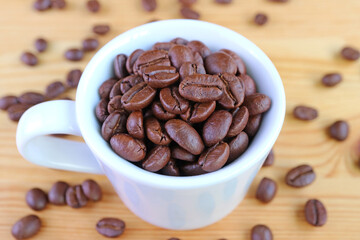 Closeup a Cup of Roasted Coffee Beans with Scattered Beans on Wooden Background