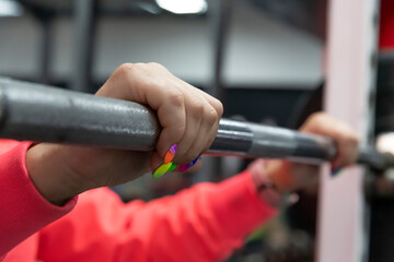 Close-up side view of female hands with bright rainbow coloured nails holding barbell before squat...