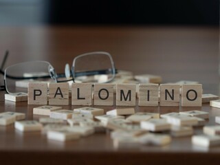 palomino word or concept represented by wooden letter tiles on a wooden table with glasses and a...