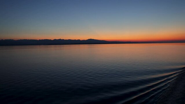 Gentle ship wake rolls in ripples on smooth water at beautiful orange sunset against deep blue sky as dusk settles over the inside passage to Alaska
