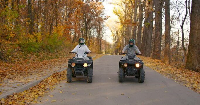 A young couple rides an ATV off-road in the autumn forest