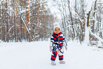 Fototapeta na wymiar Winter portrait of happy little girl wearing knitted hat and a jumpsuit outdoor in winter