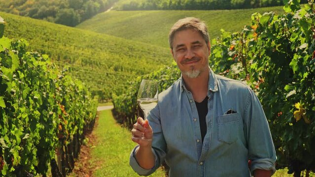 Portrait of happy vintner in vineyard during vintage holding glass of wine, tasting drinking, celebrating success.