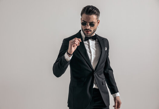 seductive young man in elegant tuxedo holding arms in fashion pose