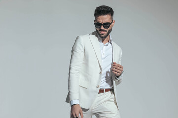 bearded fashion man wearing white suit and sunglasses and looking down